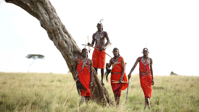 Maasai men standing beside a tree in the Maasai Mara, Kenya